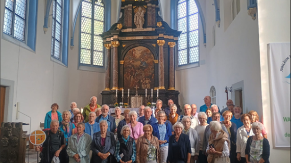Man sieht eine Gruppe älterer Menschen vor einem reich verzierten Hochaltar stehen
