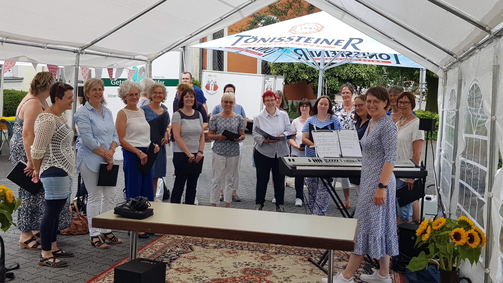 Man sieht die Frauen des Chores vor einer Bierzeltgarnitur unter einem Pavillon