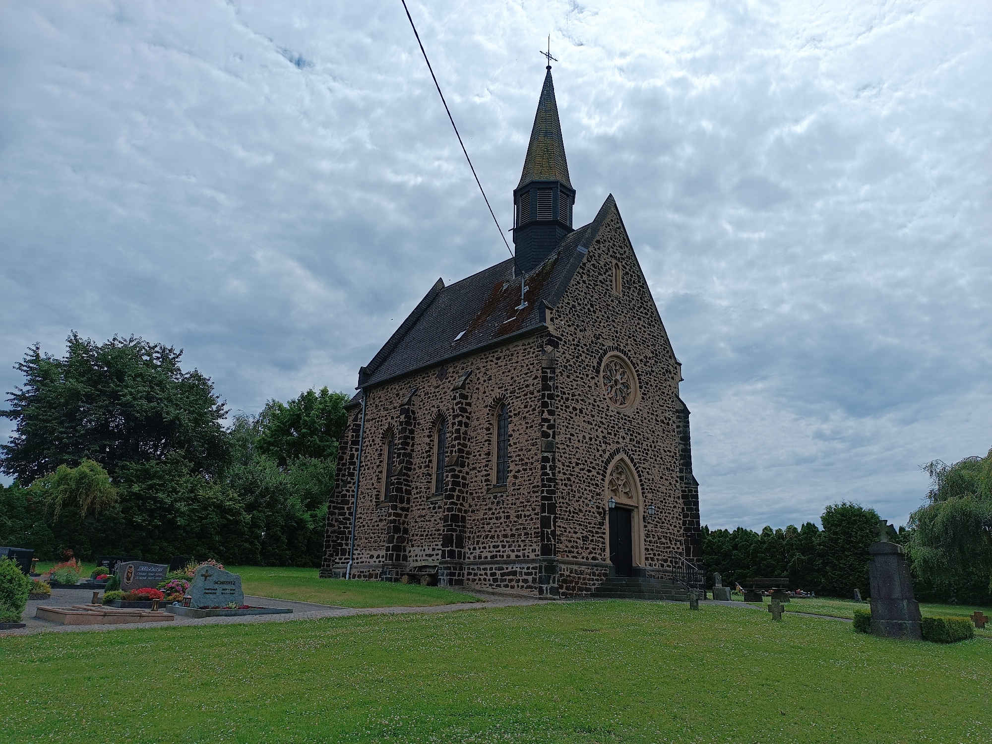 aus dunklem Sandstein gemauerte Kirche, Eingang vom Friedhof her