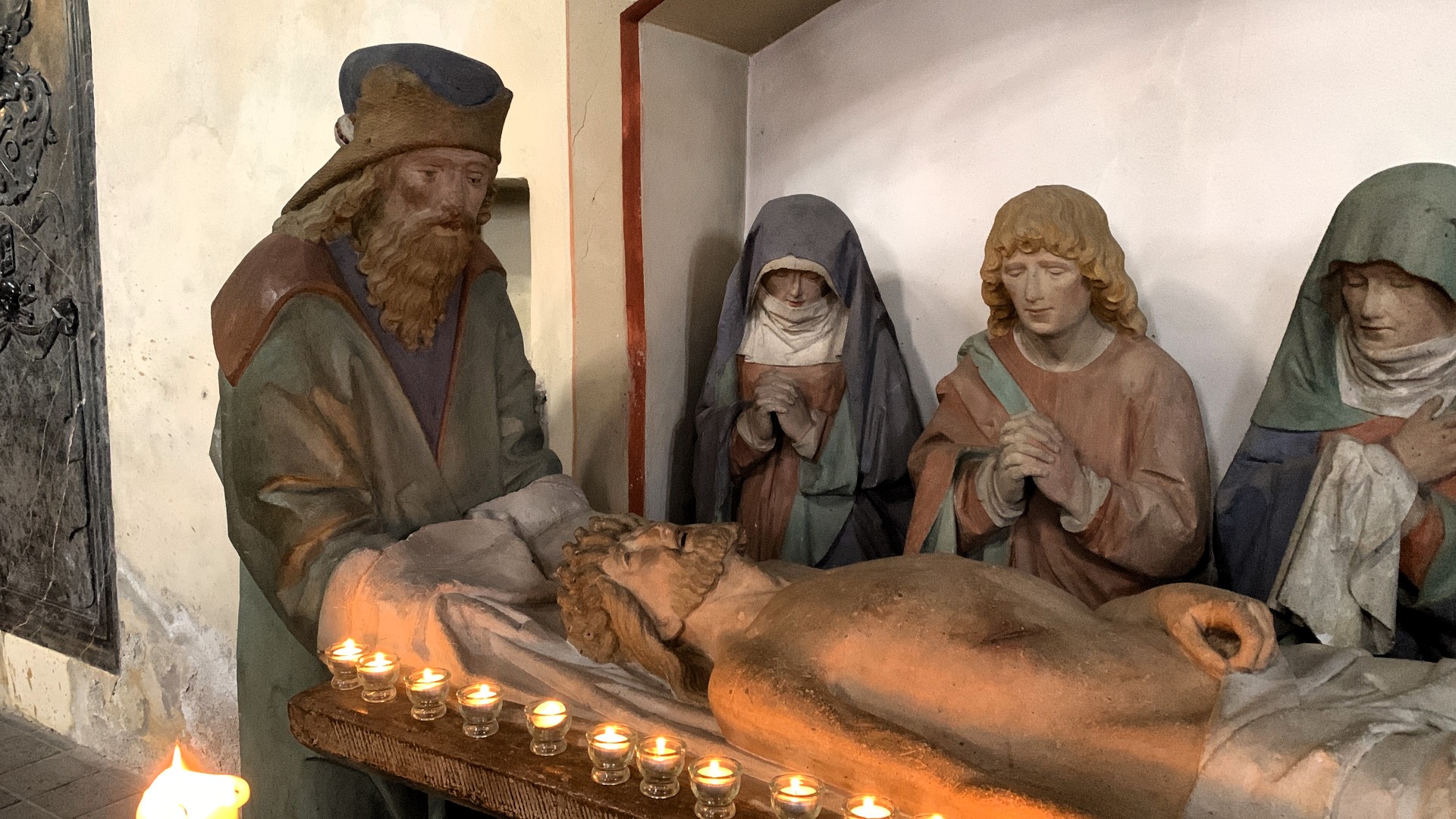 Man sieht die steinerne Grablegungsgruppe in der Kirche in Münstermaifeld mit Kerzen geschmückt
