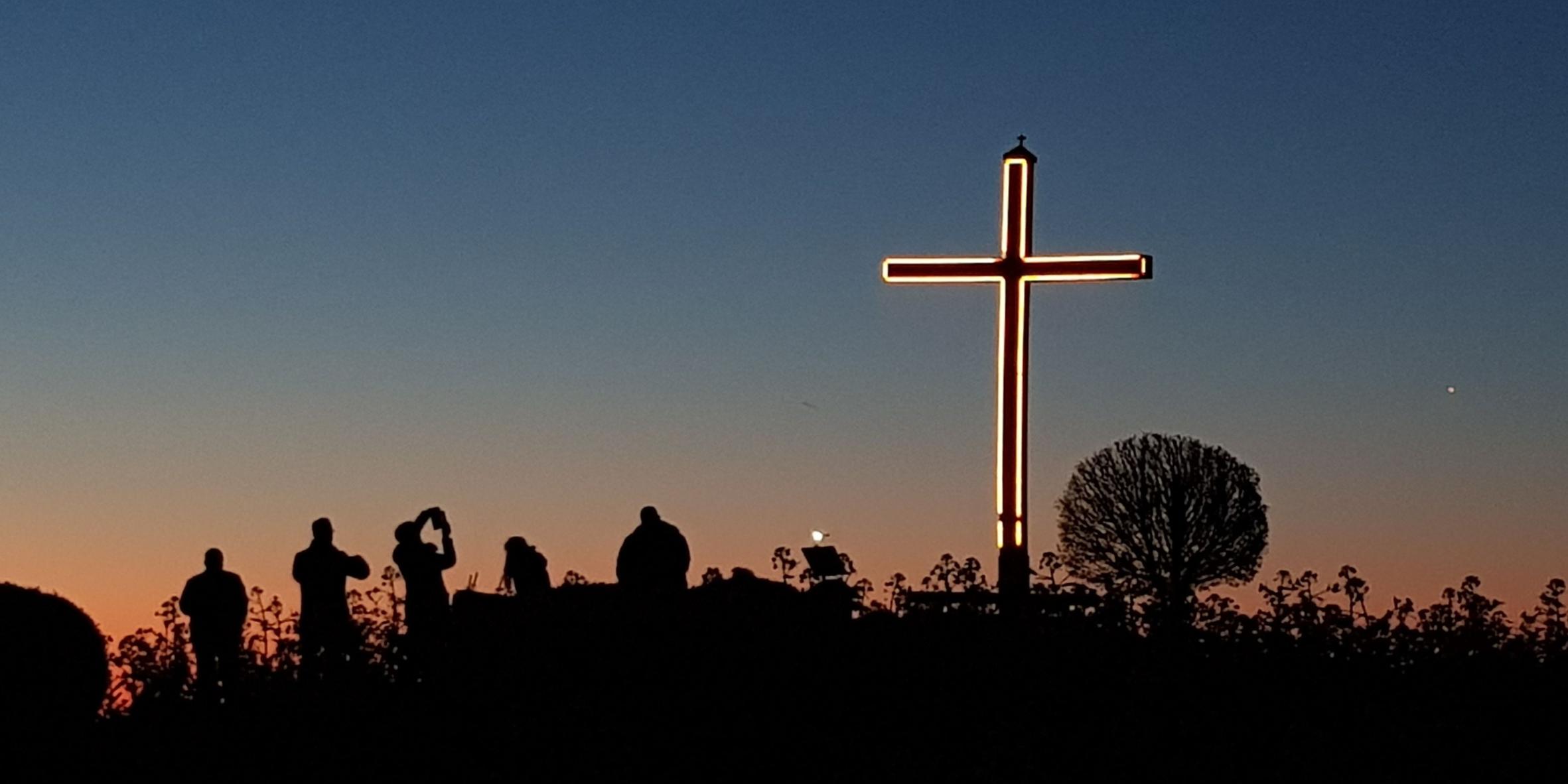 Man sieht das beleuchtete Kolliger Hochkreuz beim Nachthimmel , davor Menschen