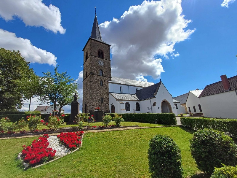 Außenansicht Kirche mit Turm rechts davor grüne Wiese mit roten Blumen