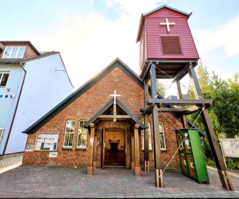 Man sieht den Eingang einer aus Holz gebauten Kirche mit einem kleinen Gebäude auf Stelzen links davor